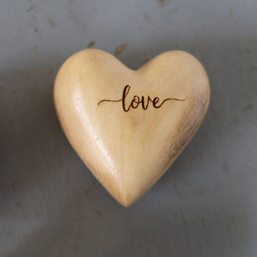Wooden heart-shaped object with 'love' engraving on a gray surface