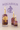 Three lit candles in decorative bottles with floral designs on a purple background with Aquarius symbol.