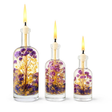 Three glass bottles with floral designs and lit candles inside on a white background