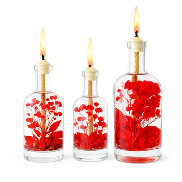 Three glass bottles with red floral contents and lit candles on a white background