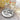 Wireless earbuds on a decorative plate with a glass of water and flowers in the background