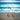 Gold earrings with blue gemstones on a sandy beach with ocean waves in the background