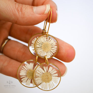 Hand holding Botanical Earrings with gold accents against a neutral background