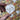 Heart-shaped cookie with a ribbon design held by a hand against a colorful heart-patterned background.