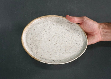 Hand holding a speckled ceramic plate against a dark background