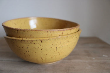 Two yellow ceramic bowls stacked on a wooden surface with a neutral background