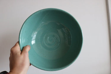 Teal ceramic bowl held by a hand against a plain background