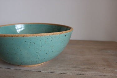 Turquoise ceramic bowl on a wooden surface with a plain background