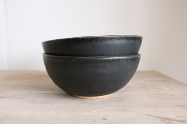 Two black ceramic bowls stacked on a wooden surface with a white background