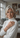 Woman in a white turtleneck standing in a living room with family photos on the wall.