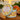 Candle in a decorative tin with fruit design on a wooden surface, sunset in the background