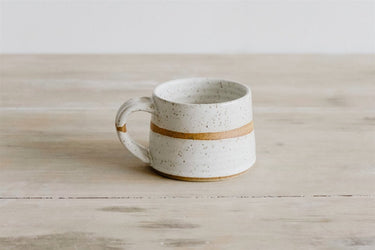 White ceramic mug with a gold band on a wooden surface