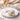 Decorative white rose with gold accents on a marble surface, surrounded by a candle and jewelry.