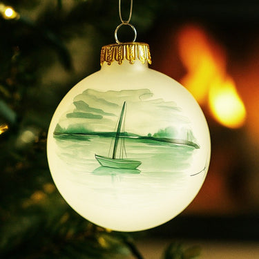 Decorative Christmas ornament with a sailboat design on a lit Christmas tree.
