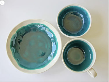 Two ceramic bowls with teal interior and beige exterior on a white background