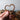 Hand holding a copper heart-shaped object with a blurred background of wooden items.