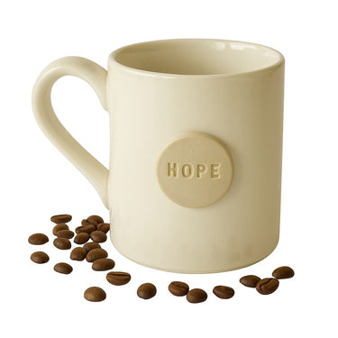Beige mug with 'HOPE' button and scattered coffee beans on a white background