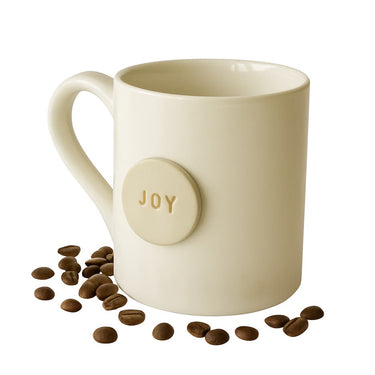 Beige mug with 'JOY' button and scattered coffee beans on a white background