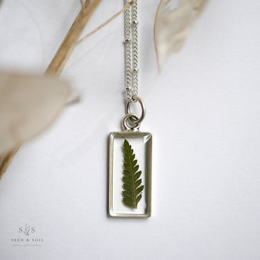 Necklace with a pendant featuring a pressed fern on a white background