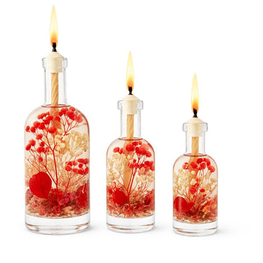 Three lit candles in decorative bottles with flowers on a white background