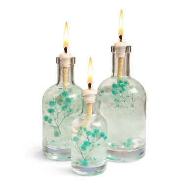 Three glass bottles with floral decorations and lit candles on a white background