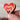Heart-shaped wooden object with a red and brown gradient held by a hand against a blurred background