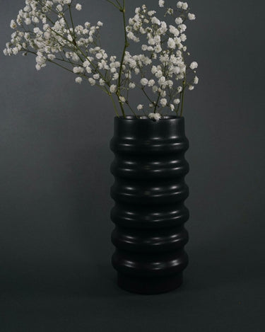 Black ribbed Ceramic Vase with white flowers against a dark background