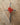 Red heart-shaped object on a cross made of metal wires, placed on a wooden surface.