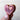 Wooden heart-shaped object with a carved design held by a hand against a light background