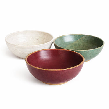 Three ceramic bowls in red, green, and beige on a white background