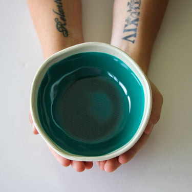 Teal ceramic bowl held by a person with tattoos on a light background