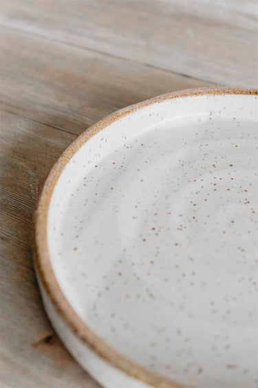 Close-up of a ceramic plate with a speckled texture on a wooden surface