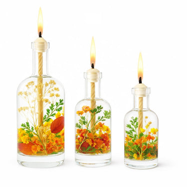 Three glass bottles with floral arrangements and lit candles on a white background