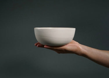 Hand holding a white ceramic bowl against a dark background