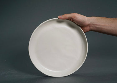 Hand holding a white ceramic plate against a dark background