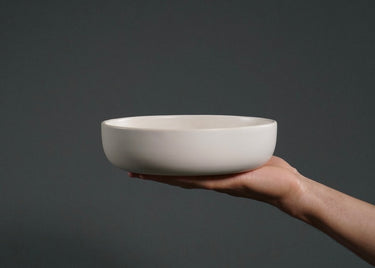 Hand holding a white ceramic bowl against a dark background