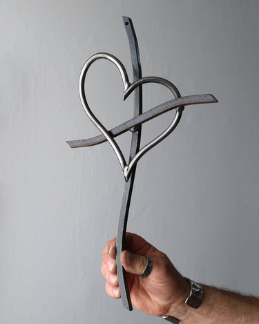 Hand holding a metal Promise Cross with an interlocking heart against a steel gray background