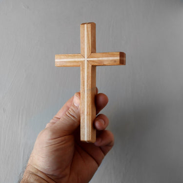 Hand holding a wooden cross against a gray background
