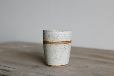 White ceramic Tumbler with brown band on a wooden surface