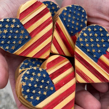 Wooden heart-shaped objects with American flag design held in a hand.