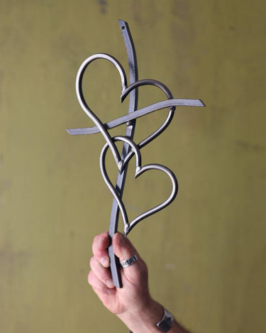 Hand holding a metal decorative cross with heart shapes against a yellow background