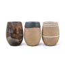 Three handcrafted ceramic tumblers with matte earth-tone glazes on a white background