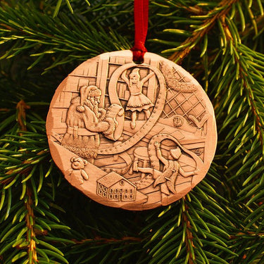 Decorative Christmas ornament with engraved scenes on a green pine branch.