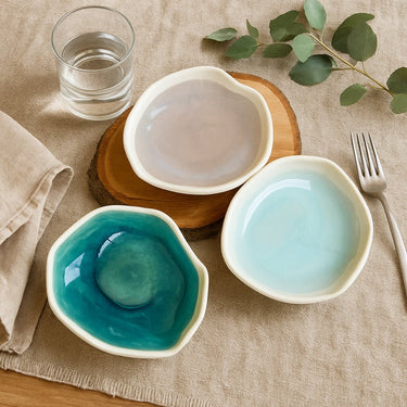 Three ceramic bowls with different colors on a table with a glass of water and a fork.
