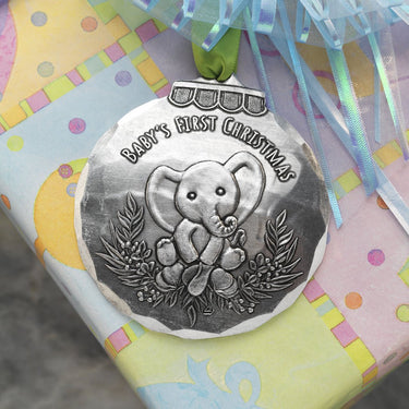 Silver baby's first Christmas ornament with elephant design on a colorful gift bag.