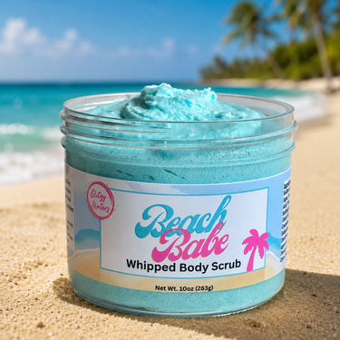Jar of 'Beach Babe' whipped body scrub on a sandy beach with ocean and palm trees in the background.