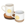 Two white mugs with gold circular designs on a wooden coaster.