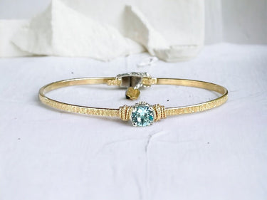 Gold bracelet with a blue Crystal on a white background