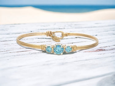 Gold bracelet with blue gemstones on a wooden surface with a beach background