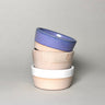 Stack of three ceramic bowls with different colored rims on a gray background